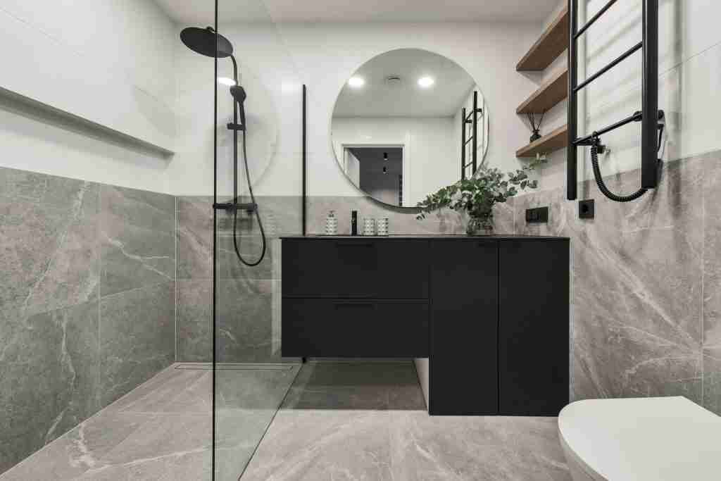 Modern minimalistic bathroom interior design with grey stone tiles, black furniture, eucalyptus in glass vase, round mirror. Aesthetic simple interior design concept. Condo Bathroom Renovations in Toronto - 6
